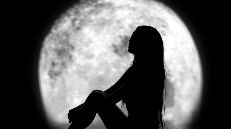 A woman sits in front of a full moon 