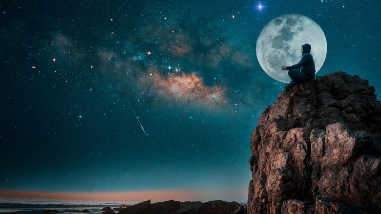 A person sitting in front of a full moon. 