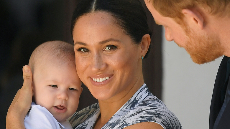 Meghan Markle holding Archie as a baby with Prince Harry looking on