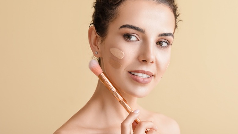 Women with foundation swatches on her face holds a pink brush