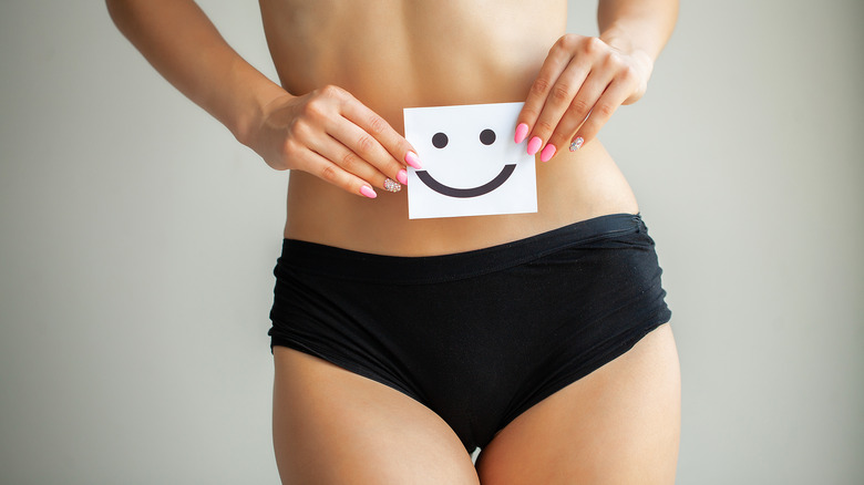 A woman holding a smiley face and wearing black panties 