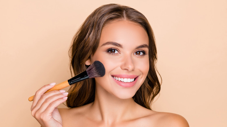 A woman applying blush on her cheeks. 