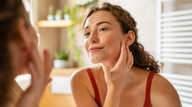 Woman touching skin, looking in mirror