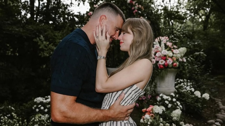 Travis Kelce and Taylor Swift embracing in a flower-filled garden