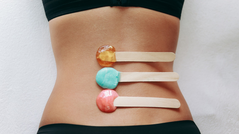 Person with three kinds of wax on popsicle sticks