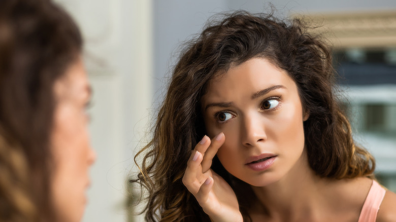 Woman analysing her under eye bags in mirror