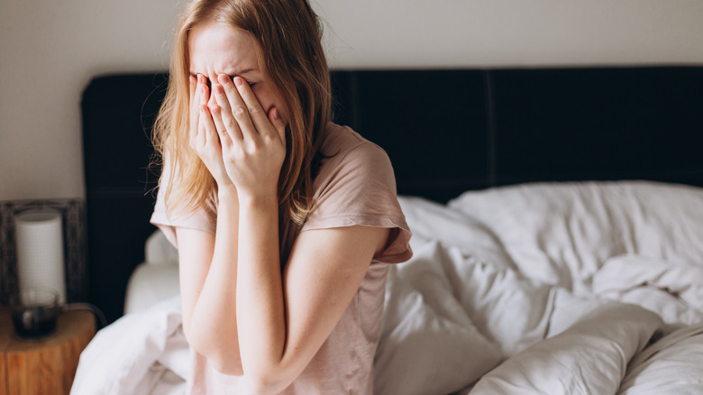 Woman sitting in bed covering her face