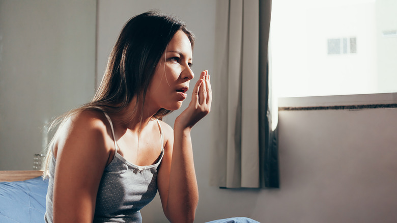 woman waking up and checking her breath in bed 