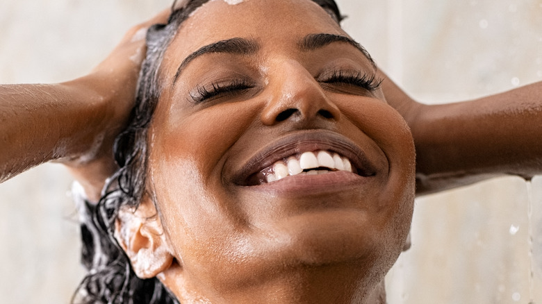 A smiling woman washes her hair in the shower.