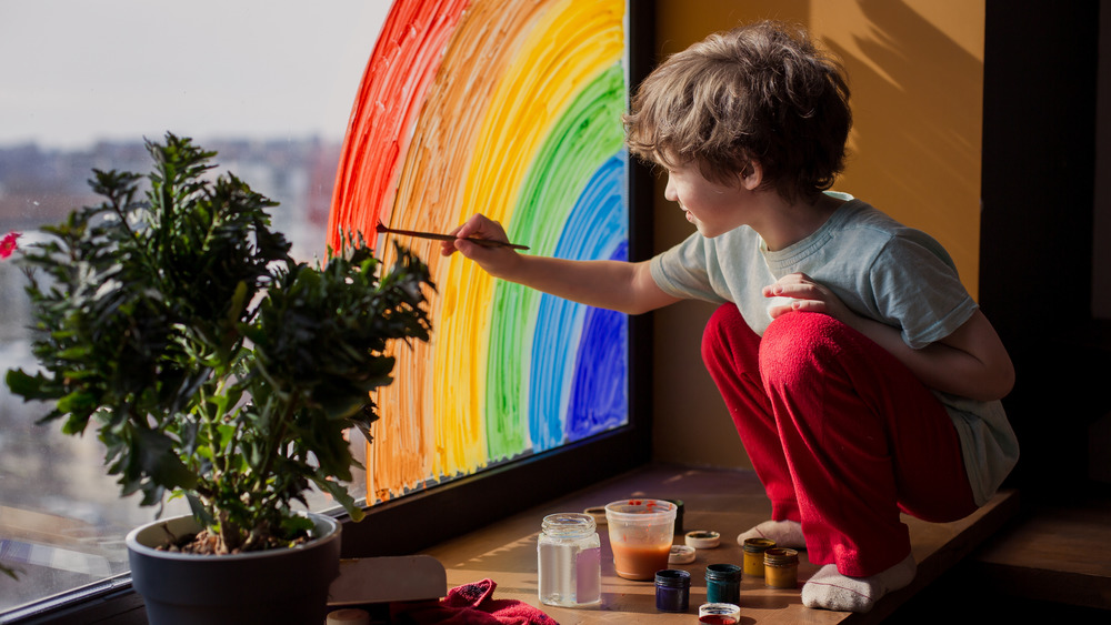 Child painting rainbow on window