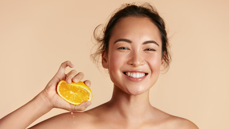 A woman with glowing skin holding an orange