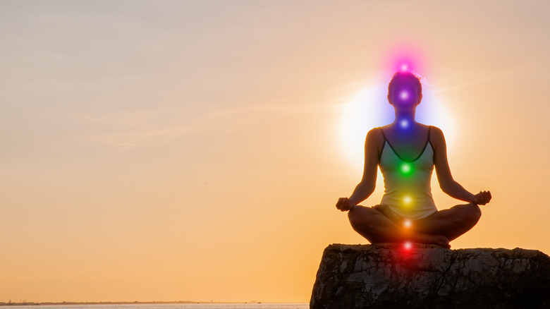 A person meditating with their chakras lit up 