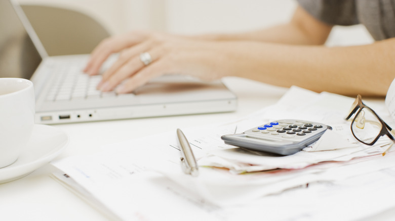 Woman typing with calculator nearby