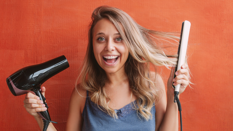 A woman holding a hair dryer and flat iron 