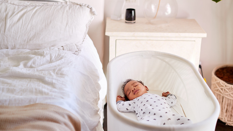 Baby in cradle next to adult bed