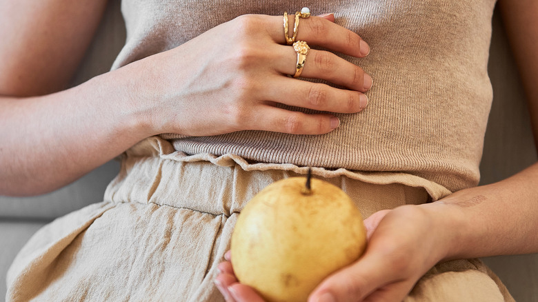 closeup of person in beige top and beige pants holding an apple