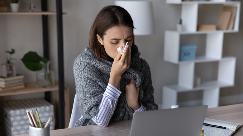 Woman at desk blowing nose