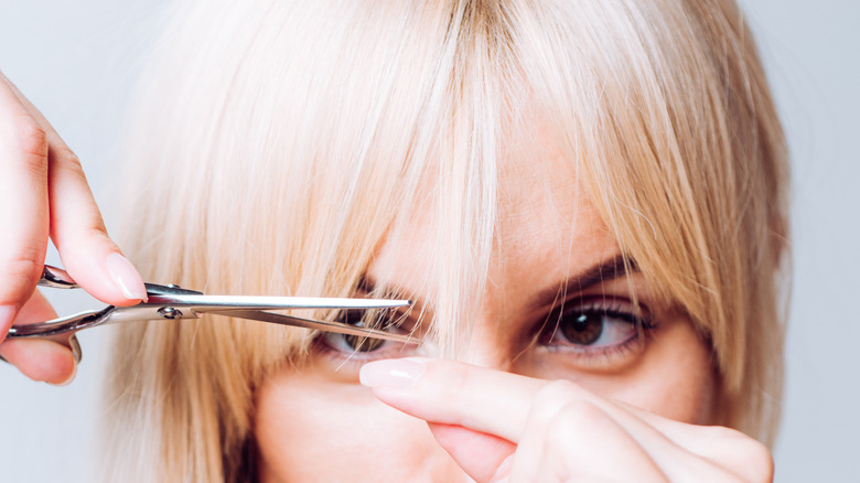 Blonde woman holding pair of scissors to her bangs