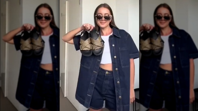 Woman wearing denim top and shorts and holding up sandals