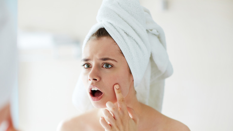 A woman noticing her acne in a mirror