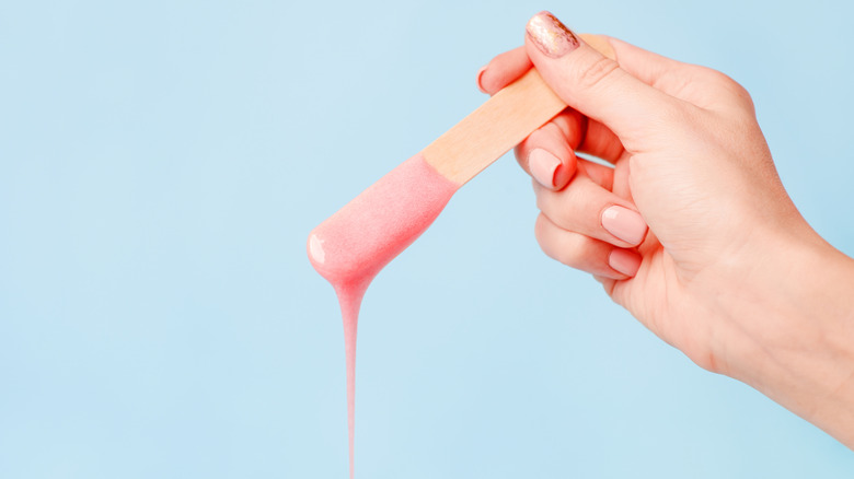 Hand holding wooden stick with sugaring paste