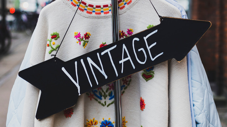 A sweater hung outside of a vintage store with a sign hanging on it