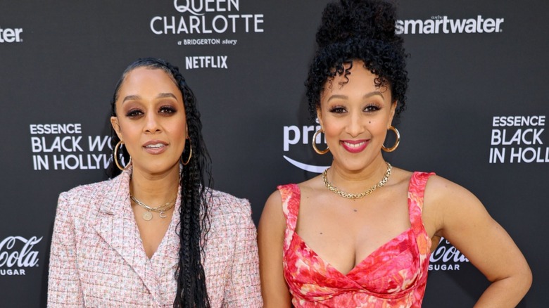 Tia and Tamera Mowry posing and smiling in front of a black background.