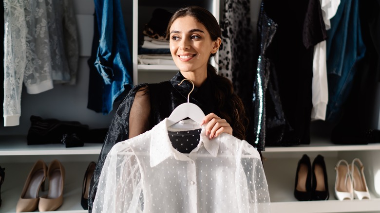 woman holding shirt in front of closet