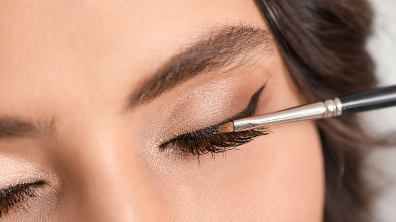 Woman drawing on winged eyeliner with a brush