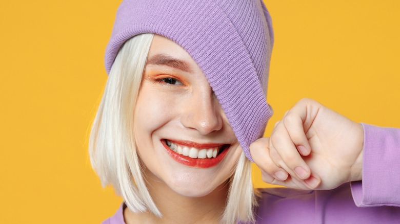 Woman with orange makeup pulls purple beanie over her face