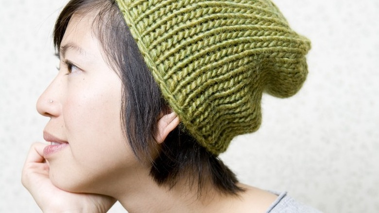 A woman with short hair wears a slouchy green beanie 