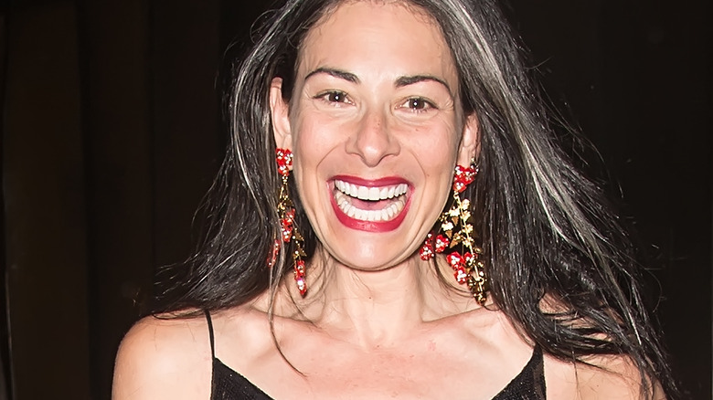 Stacy London smiling in red dangle earrings and red lipstick