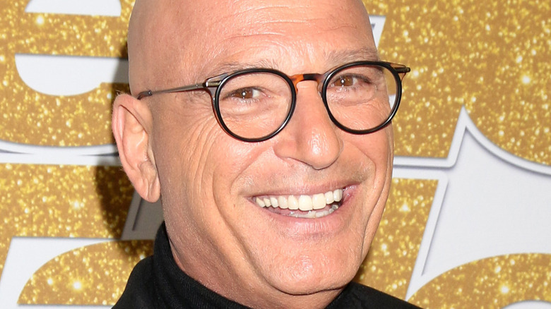 Howie Mandel smiles with black framed glasses.