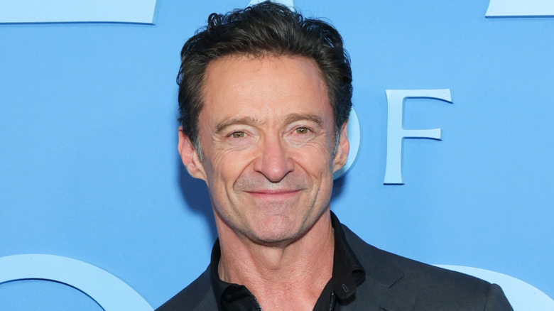 Hugh Jackman smiling while posing at an event in a dark suit