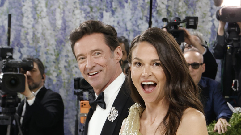 Hugh Jackman wearing a black tuxedo and suit and Sutton Foster wearing a sparkling gold dress with shocked expressions on their faces