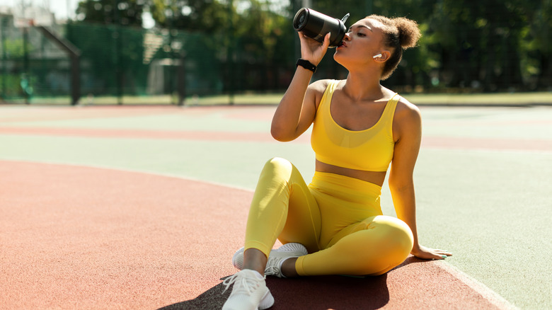 Woman sitting on a basketball court drinking water