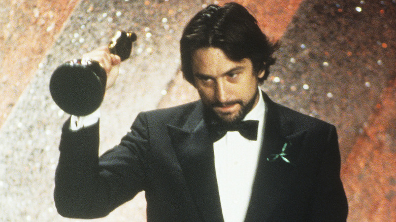 A young Robert De Niro holding up an Academy Award in a tuxedo