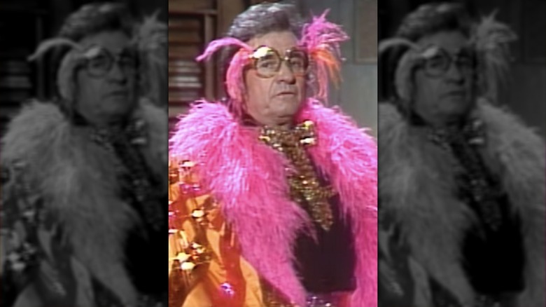 Johnny Cash, wearing a feather boa and round glasses, introducing Elton John on "Saturday Night Live" in 1982