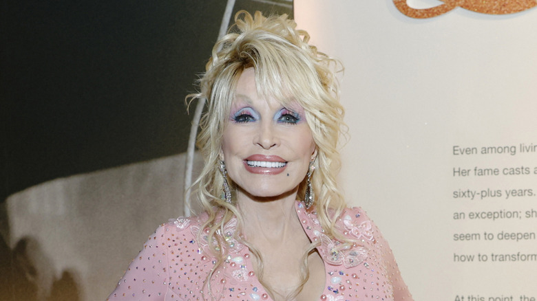 Dolly Parton smiling while posing in a pink beaded jumpsuit