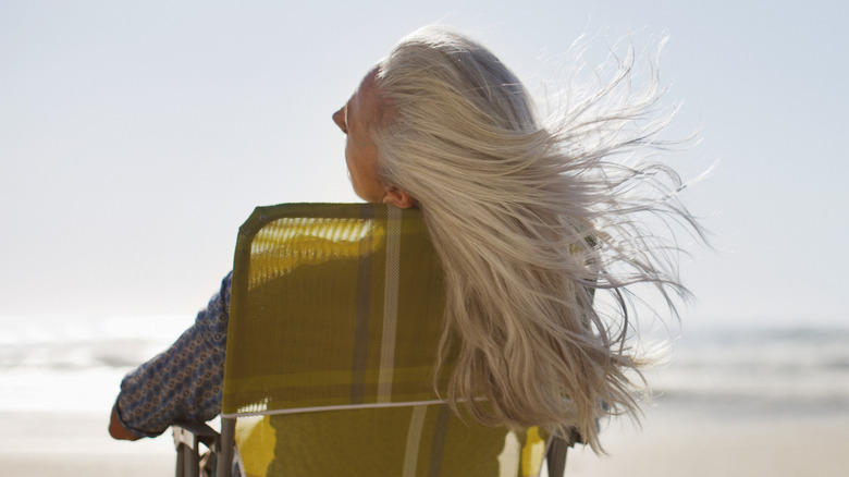 Person sitting in a beach chair on the beach with gray hair blowing in the wind