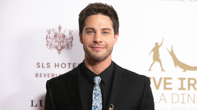 Dean Geyer posing in a black suit and shirt with a patterned tie on the read carpet for a Steve Irvin Gala Dinner