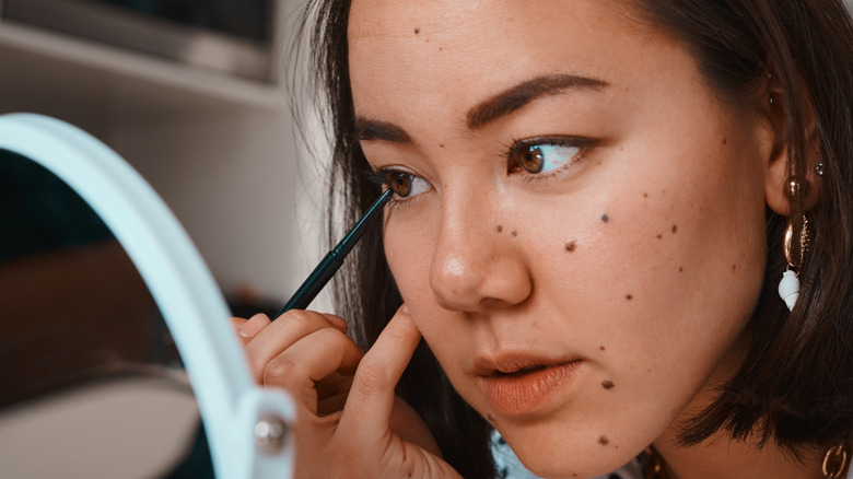 Woman applying eyeliner in the mirror