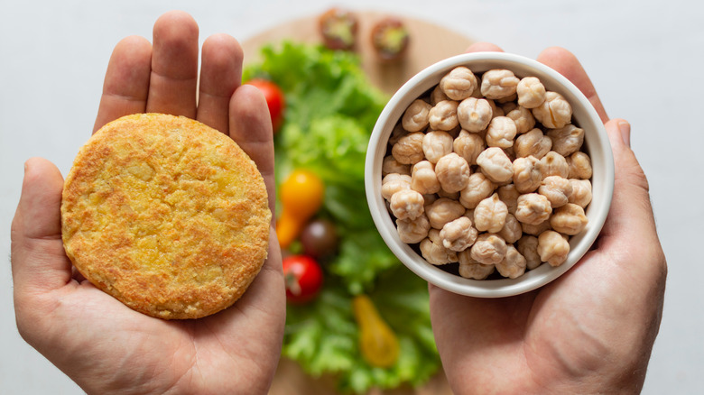 Hands holding a vegan burger and chickpeas