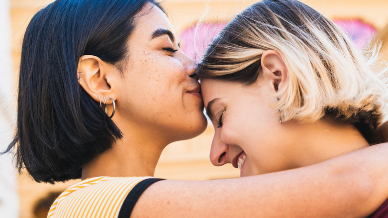 woman kissing girlfriend's forehead while embracing