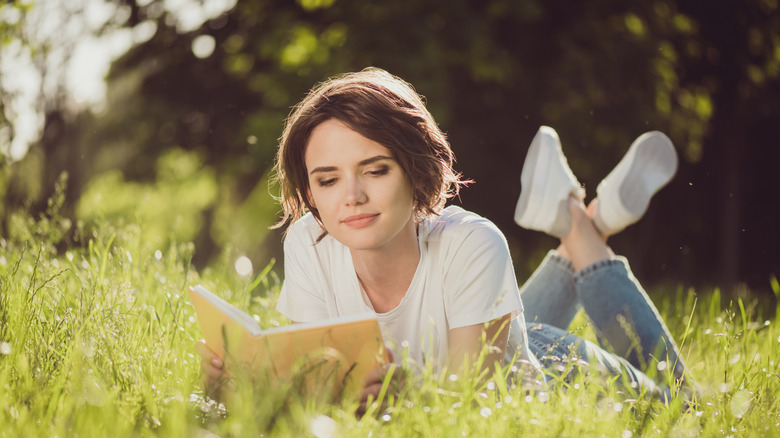 woman laying in grass reading a book