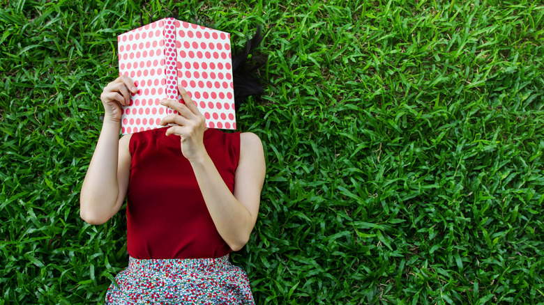 woman laying in grass holding up book