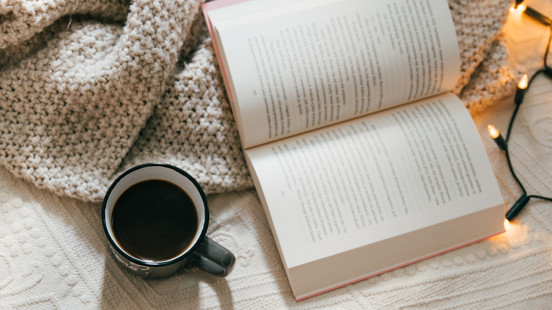 book on a bed with a blanket, lights, and coffee