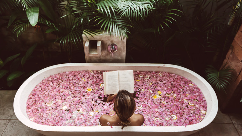 woman in tub full of rose petals reading a book