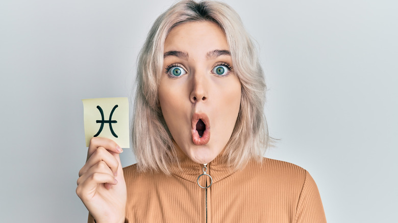 Surprised-looking woman holding Pisces symbol