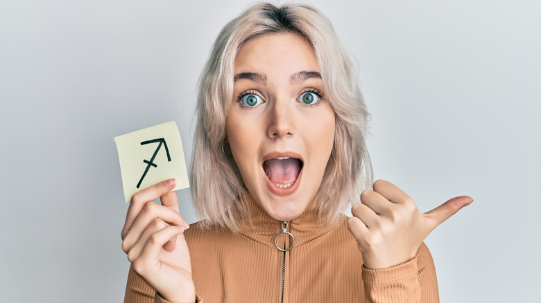 A woman holding a card with a Sagittarius sign on it. 